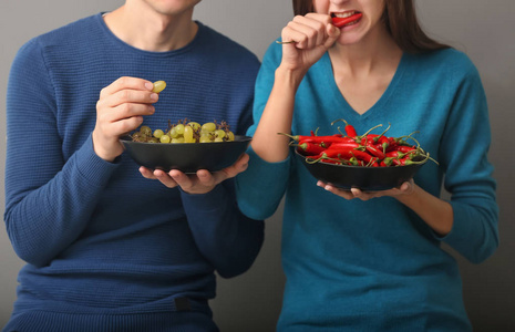 年轻夫妇在灰色背景下吃葡萄和辣椒