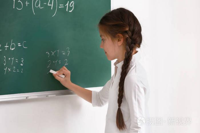 可爱的女孩在教室的黑板上写字