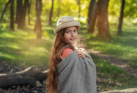 日落时留着长发的漂亮女孩在森林里。 一个女孩的肖像。 裹在毯子里的孩子