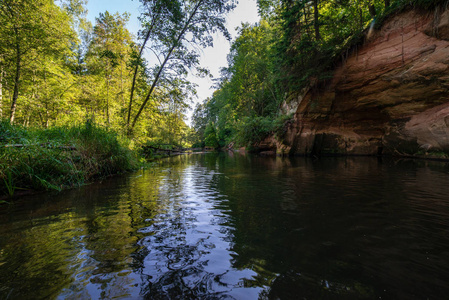 夏日的水在平静的河流中，封闭在砂岩悬崖和干燥的木材的森林中。 布拉斯拉拉特维亚河中的暗水