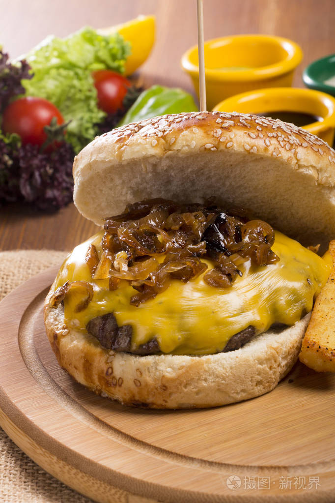 关闭自制烤芝士汉堡与油炸焦糖洋葱和融化切达奶酪与手指薯条洋葱环