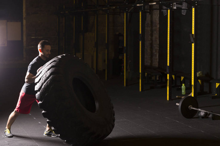 黑色衬衫男人在健身房里翻着沉重的大轮胎。