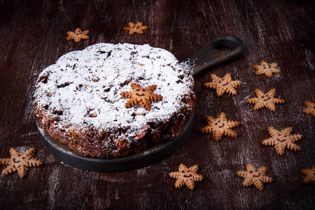 传统的圣诞蛋糕平底锅和姜饼饼干，形状为雪花，放在深色的木桌上