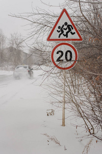 危险的冬季道路上的汽车暴风雪限速标志20和白色背景上谨慎的行人