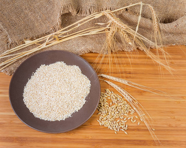 粗磨大麦的顶部景色，在棕色的盘子上，全麦粒，一束大麦的耳朵在麻布和竹木表面上