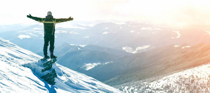 独自游客站在雪山顶上的剪影，在阳光明媚的冬日，举起双手欣赏风景和成就。 冒险户外活动健康的生活方式。