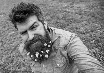 时髦的人在眨眼的脸上坐在草地上, 弥散。人与胡子喜欢春天, 绿色草甸背景。小塞伦丁花胡子拿自拍照片的家伙。春季季节概念