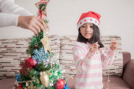 亚洲小女孩带着一起装饰圣诞树，为快乐的聚会选择焦点野