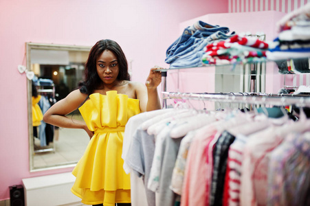 时尚的非裔美国妇女在黄色的阴暗处摆姿势在粉红色的商店，并选择衣服。
