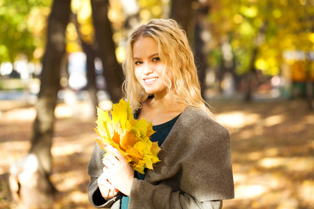 一位年轻漂亮的金发女子的肖像，穿着灰色外套，在秋街的背景下。