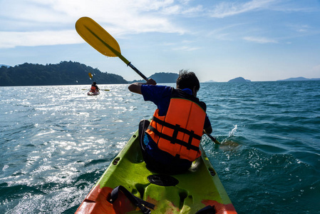 亚洲青少年在有蓝海和岛屿背景的皮艇上划船。