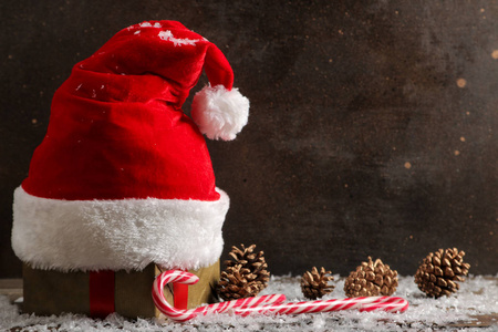 红色圣诞老人帽子，锥和雪在深棕色的背景。 有文字的空间。 圣诞节。 新年。