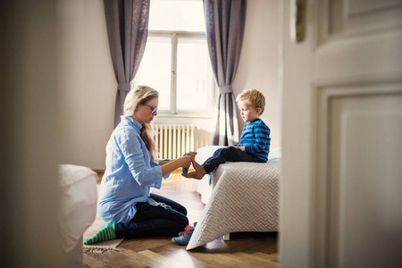 一位年轻的母亲在卧室里给幼儿儿子穿上袜子