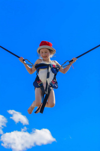 孩子们在蹦床上跳，用橡胶绳在蓝天上。 冒险和极限运动。 夏季娱乐跳跃的概念。