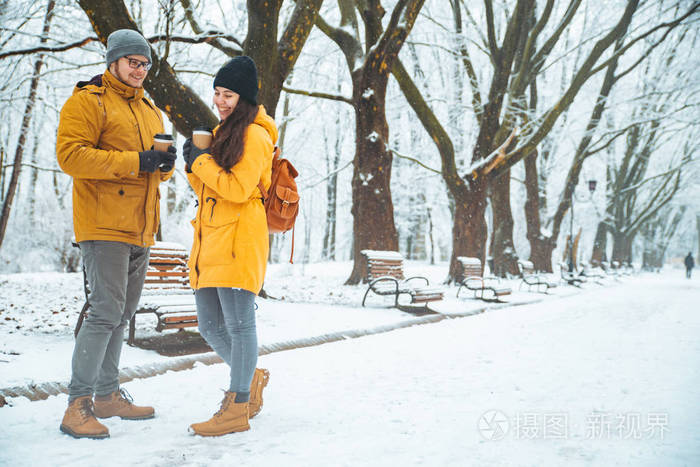 一对夫妇在下雪的城市公园边散步，谈论社交。 冬天的浪漫约会。 圣诞节快到了