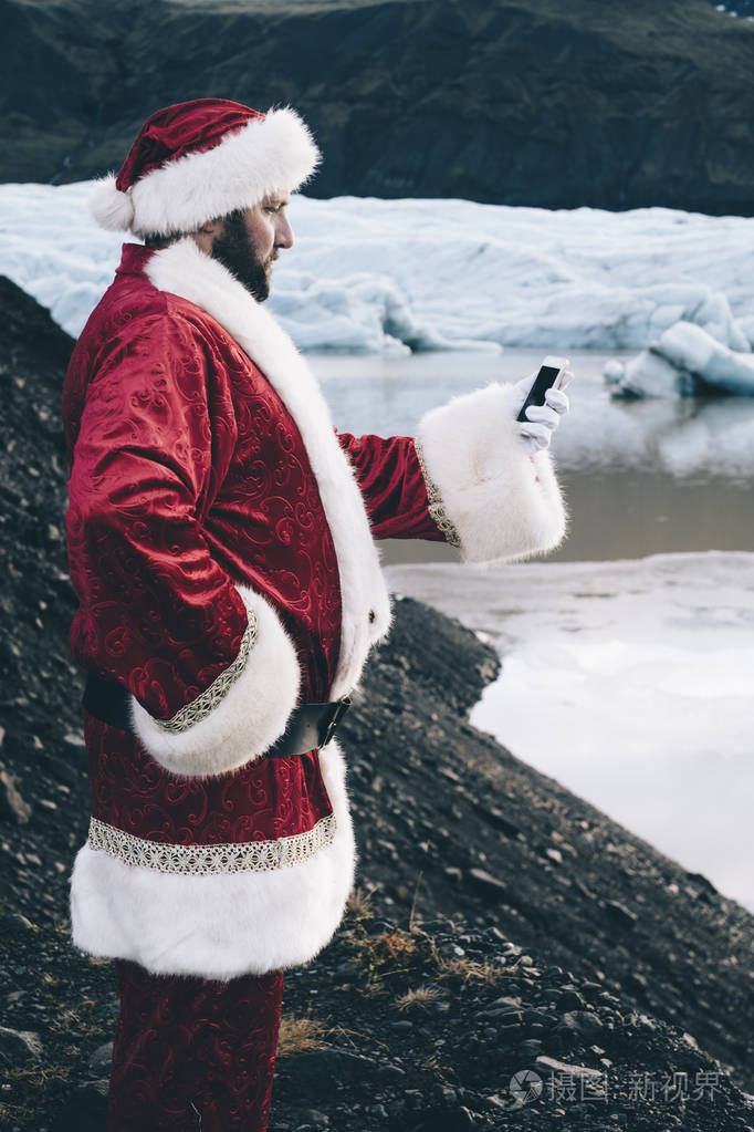 传统风格的正宗圣诞老人看着他的手机左手在冰岛冰川照片-正版商用图