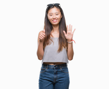 年轻的亚洲女人戴着太阳镜，在孤立的背景上，用手指第六，同时微笑，自信和快乐。