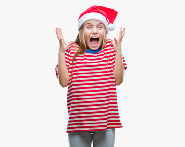 年轻漂亮的女孩戴着圣诞帽，在孤立的背景上庆祝疯狂，并惊讶于成功，举起手臂睁开眼睛尖叫兴奋。 赢家概念