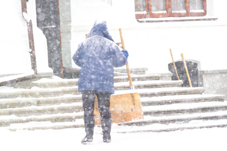 一个女人在雪灾中铲雪。清洁楼梯