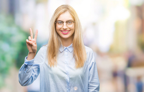年轻漂亮的金发商务女性戴着眼镜，戴着孤立的背景，用手指举着第二个手指，微笑着自信和快乐。