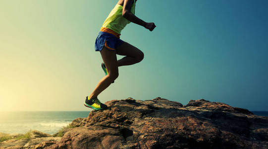 年轻的健身女子跑步者跑到海边的岩石山顶