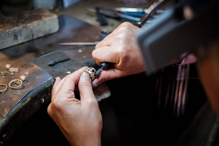 珠宝商在一个真正的珠宝车间的旧工作台上擦亮一枚金戒指