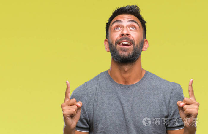 成年西班牙裔男子在孤立的背景上惊讶和惊讶地抬头,手指和举起的手臂.
