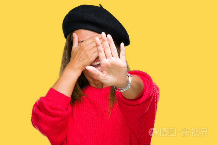 中年妇女穿着时尚贝雷帽在孤立的背景上用手遮住眼睛用悲伤和恐惧的