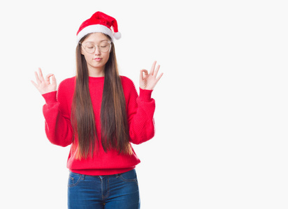 年轻的中国妇女在孤独的背景下，戴着圣诞帽，放松和微笑，闭着眼睛，用手指做冥想手势。瑜伽概念。