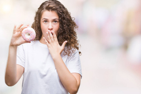 年轻的黑发女孩吃甜甜圈，在孤立的背景上，用手捂住嘴，因错误而，害怕在沉默，秘密的概念