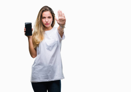 年轻漂亮的金发女郎用张开的手在孤立的背景上展示智能手机屏幕，用严肃而自信的表情防御手势做停止标志