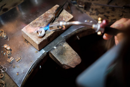 珠宝在工作台上焊接一个金环，焊枪上的火焰在真正的珠宝车间