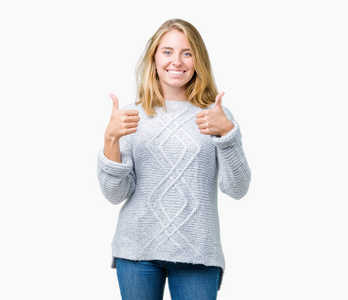 美丽的年轻女子穿着冬季毛衣，在孤立的背景上成功标志，用手做积极的手势，竖起大拇指微笑和快乐。用欢快的表情看着镜头，胜利者的手势.