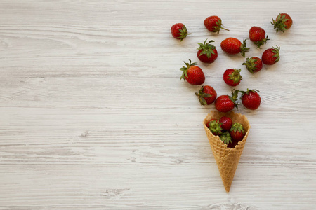 华夫饼甜冰淇淋锥与草莓在白色木制表面俯视。 平躺在上面。 复制空间。