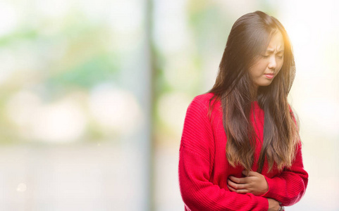 年轻的亚洲女人穿着冬天的毛衣，在孤立的背景上，手放在肚子上，因为恶心痛苦的疾病感觉不舒服。 疼痛的概念。