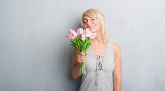白种人成年妇女在灰色的格朗格墙上抱着粉红色的花，聪明的脸上带着自信的表情，严肃的思考着