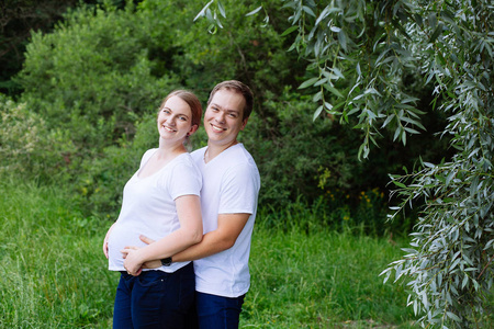 快乐的孕妇和她的丈夫在夏季公园