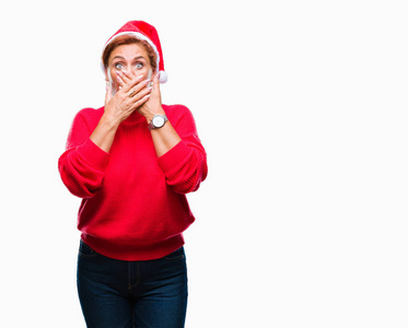 迷人的高级白种人红发妇女戴着圣诞帽，在孤立的背景下震惊地用手捂住嘴，因为错误。 秘密概念。