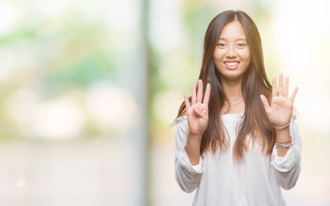 年轻的亚洲女人在孤立的背景上，用手指数字9，同时微笑，自信和快乐。