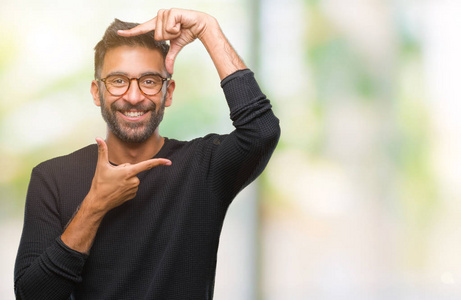 成年西班牙裔男子戴着眼镜，在孤立的背景上微笑，用手和手指制作框架，用快乐的脸。 创造力和摄影理念。