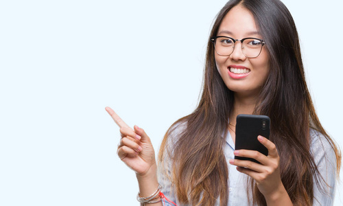 年轻的亚洲女人用智能手机在孤立的背景上发短信，非常高兴地用手和手指指向一边