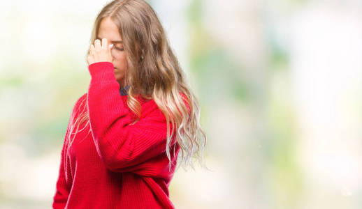 美丽的年轻金发女人穿着冬季毛衣，在孤立的背景下疲惫地鼻子和眼睛，感到疲劳和头痛。 压力和挫折的概念。
