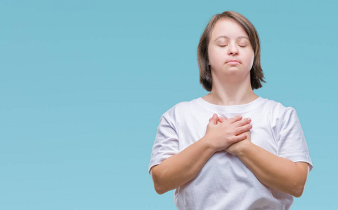 年轻的成年妇女患有唐氏综合症,在孤立的背景上微笑,双手放在胸部,闭