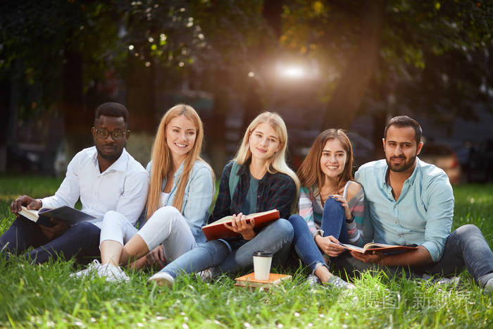 在大学校园绿色草坪上共同坐着的混合竞赛学生群体