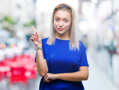 年轻的金发女人在孤立的背景上，脸上挂着一个大大的微笑，用手和手指指向一边，看着相机。