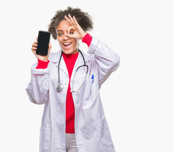 年轻的美国医生女士使用智能手机在孤立的背景和快乐的脸微笑，做好的标志，手在眼睛看通过手指。