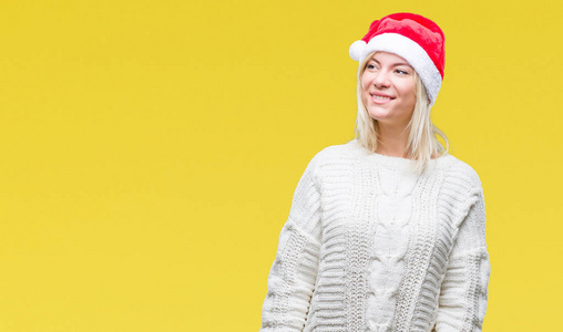 年轻漂亮的金发女人戴着圣诞帽，在孤立的背景上看着一边，脸上带着微笑，自然的表情。 自信地笑着。