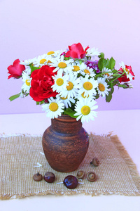 陶罐里的白色雏菊和红色玫瑰花束正在被采摘。 丁香背景上的花盆里的花。 桌上花瓶里的洋甘菊和红玫瑰