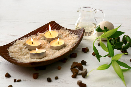 在水疗沙龙的白色木桌上放有海盐的盘子和燃烧的蜡烛