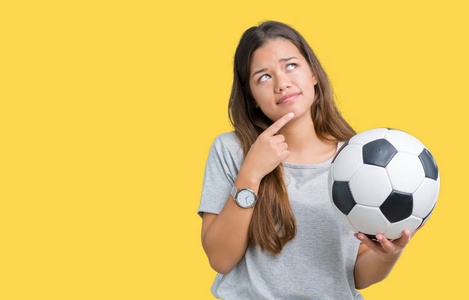年轻漂亮的黑发女人抱着足球在孤立的背景下严肃的脸思考问题很困惑的想法
